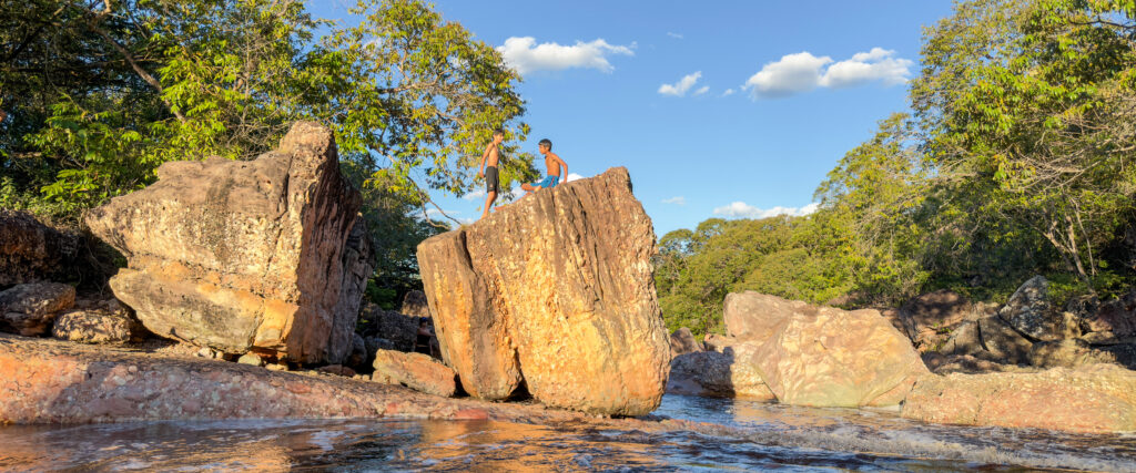 Two boys on the rocks of Serrano, in Lençóis, Chapada Diamantina, with a blue sky in the background.