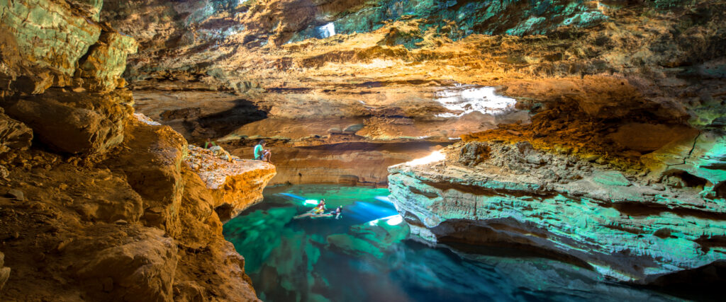 Pessoas nadando nas águas transparentes do Poço Azul sob um feixe de luz natural na Chapada Diamantina.