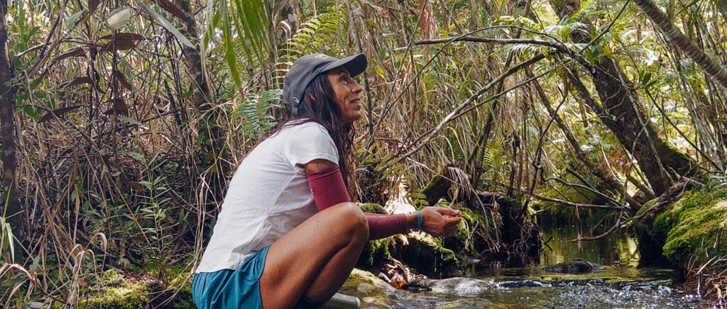 Guia Cris Pascoli bebendo água de uma fonte natural e observando a vegetação durante uma caminhada no Vale do Pati, na Chapada Diamantina.